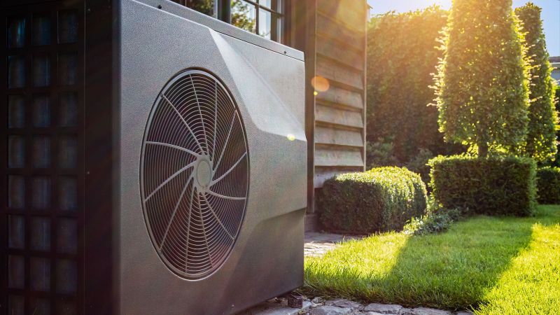 Das Bild zeigt eine Wärmepumpe vor einem Haus im Sonnenschein.