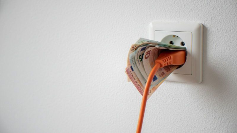 Das Bild zeigt eine Steckdose und ein Kabel mit Stecker, dazwischen Geldscheine. Das steht symbolisch für das Thema Strombepreisung.