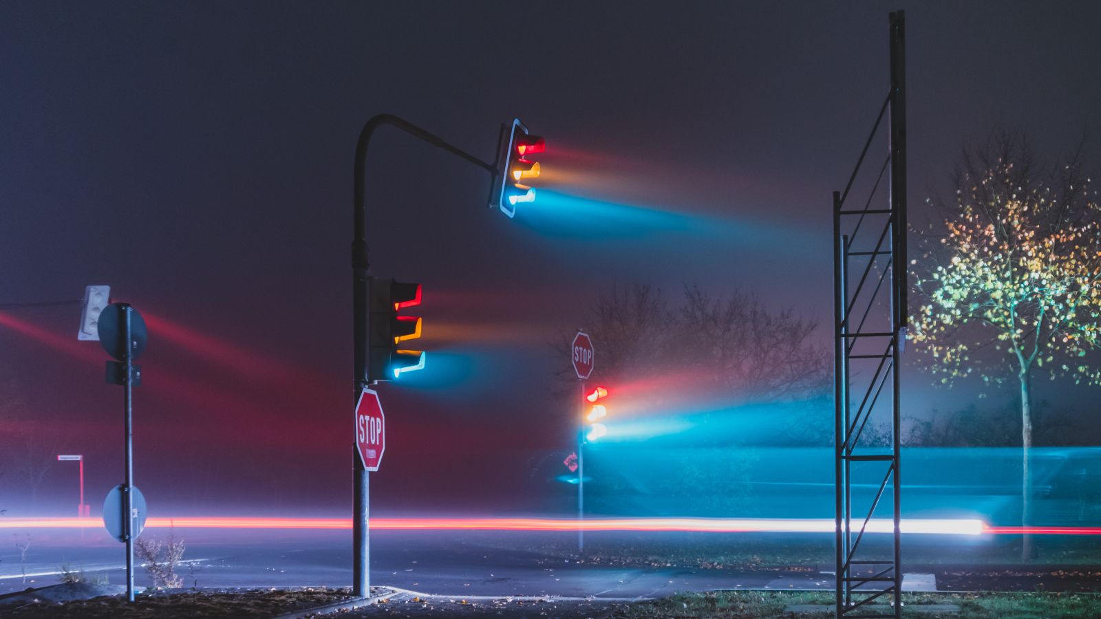 Das Foto zeigt eine leere Straße im Nebel, auf der drei Ampeln stehen, deren drei Lichter grün, gelb und rot allesamt leuchten. 