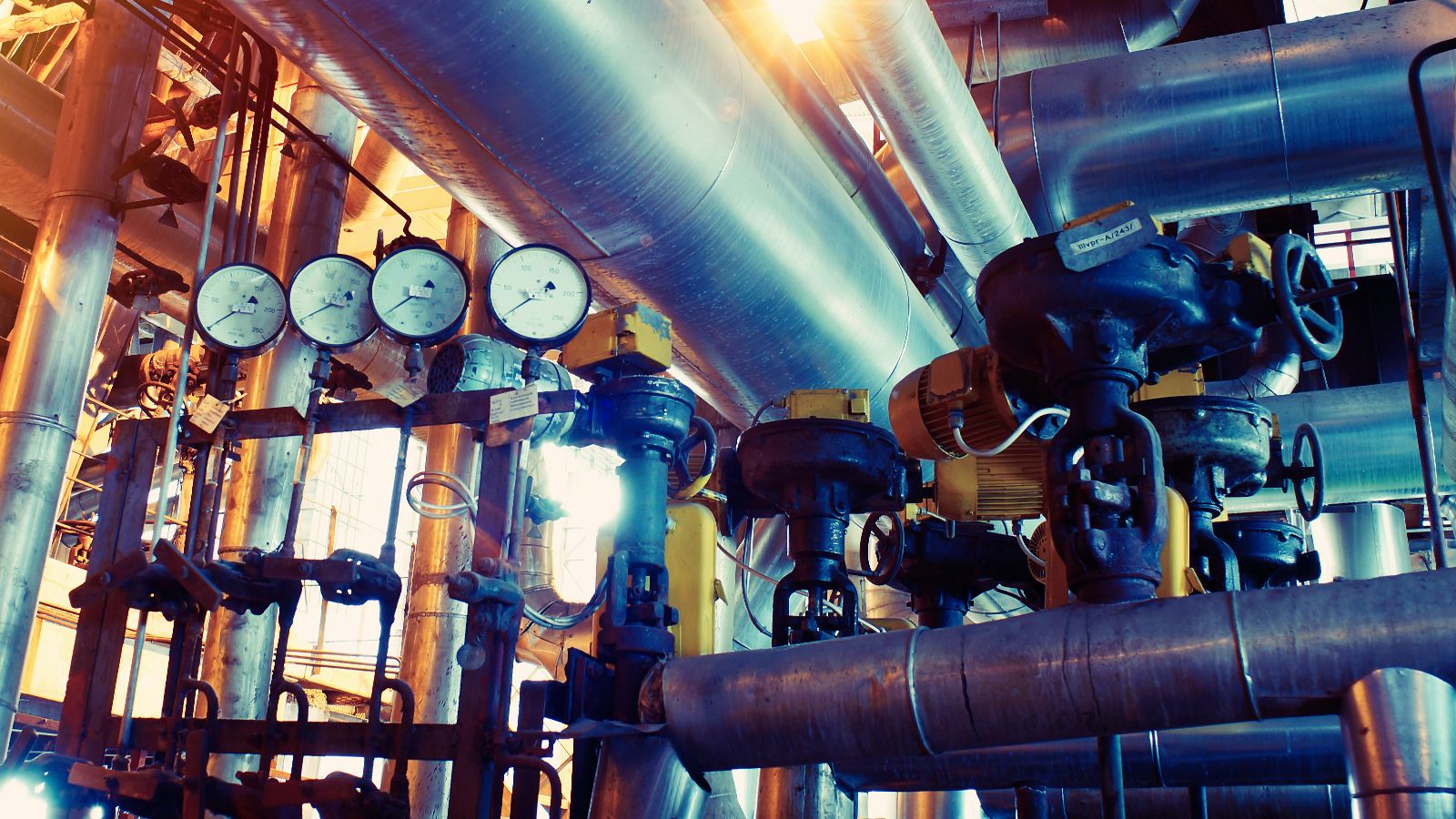 Das Bild zeigt einen Industrieraum mit Stahlrohrleitungen, Ventilen und Pumpen.