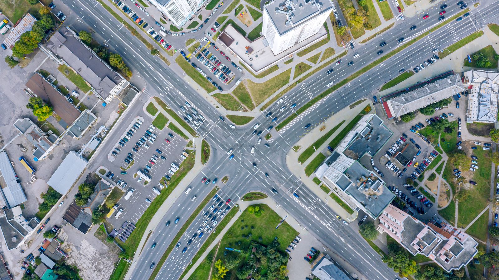 Das Bild zeigt eine Stadtkreuzung mit Fahrzeugen umgeben von Häusern von oben.