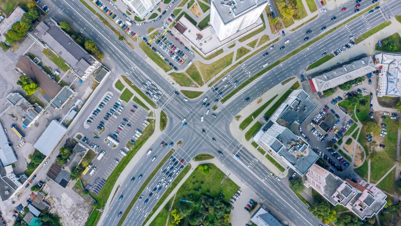 Das Bild zeigt eine Stadtkreuzung mit Fahrzeugen umgeben von Häusern von oben.