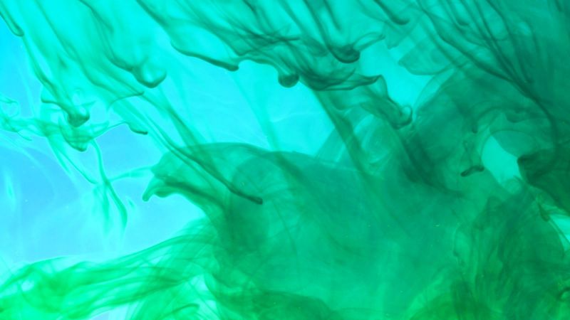 Das Bild zeigt grüne Farbe in Wasser aufsteigen - vor einem blauen Hintergrund. 