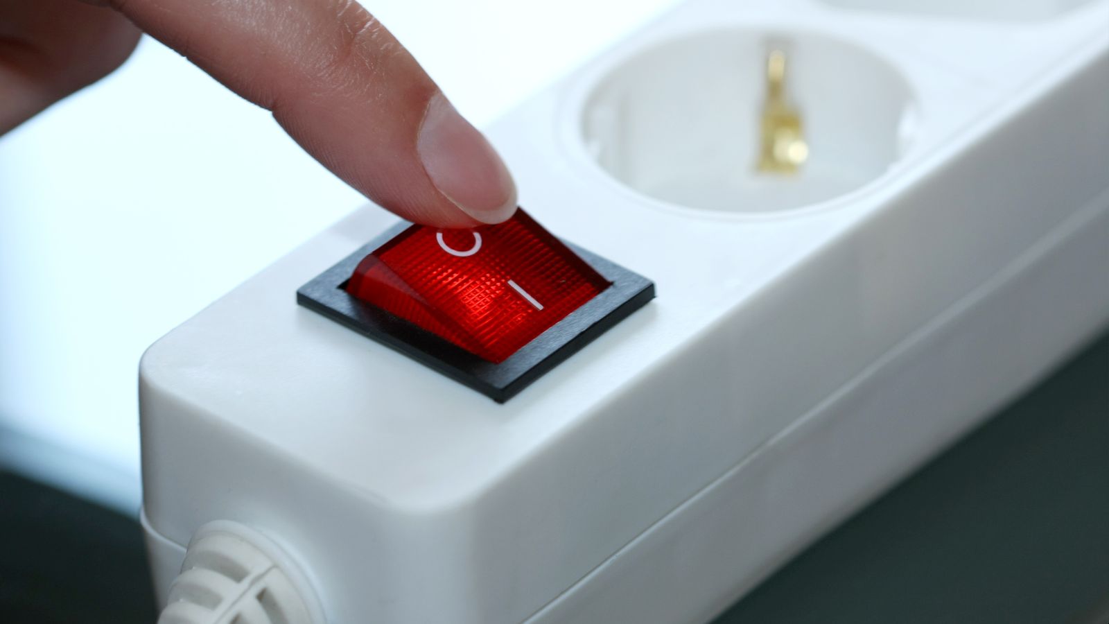 Das Bild zeigt einen Finger, der dabei ist, den Schalter einer Steckdosenleiste auszuschalten.