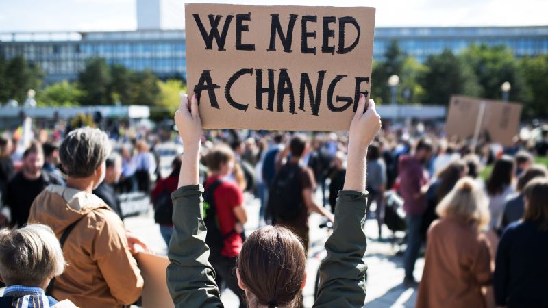 Das Bild zeigt eine Frau von hinten, die als Teilnehmerin an einem Protest ein Plakat hochhält.