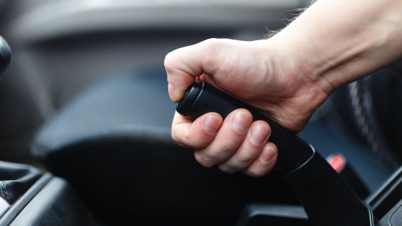 Das Bild zeigt eine Hand, die an einer Handbremse in einem Auto zieht.