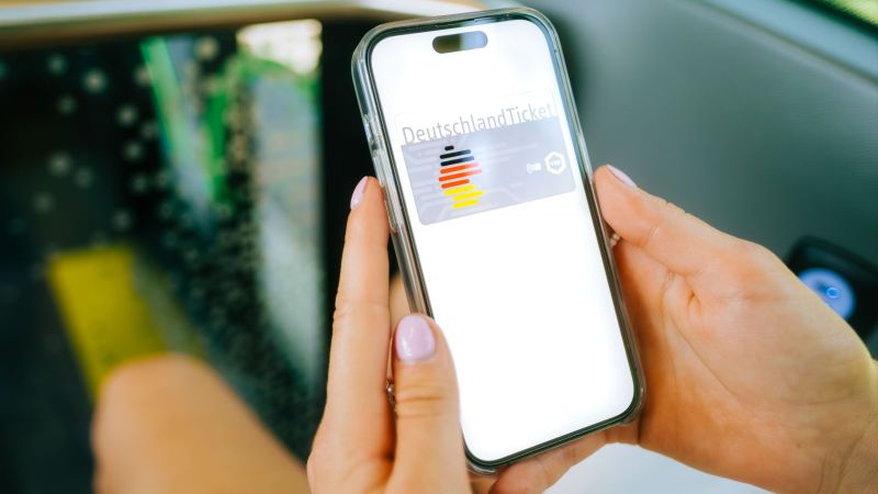 Das Bild zeigt ein Mobiltelefon mit dem Deutschlandticket in den Händen einer Person, die in einem Bus oder einer Straßenbahn sitzt.