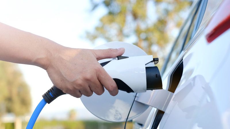 Das Bild zeigt eine Hand, die ein weißes E-Auto lädt.