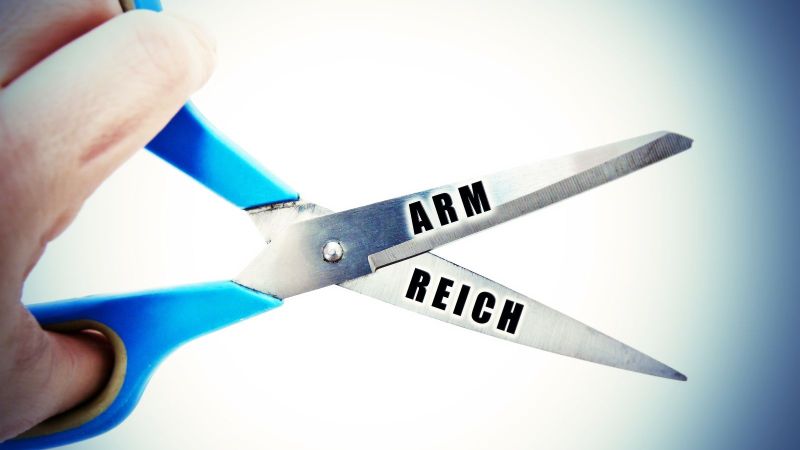 Das Bild zeigt eine Hand in Nahaufnahme, die eine Schere hält, auf deren Klingen die Wörter 