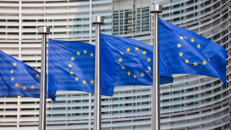 Das Bild zeigt mehrere Europa-Flaggen, die vor einem Gebäude in Brüssel wehen.