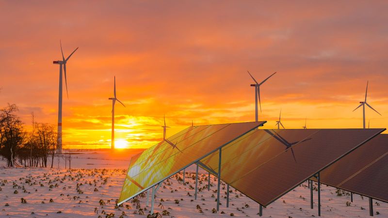 Das Bild zeigt Windräder und Solarpanels auf einem Feld bei einem winterlichen Sonnenuntergang mit Schnee.