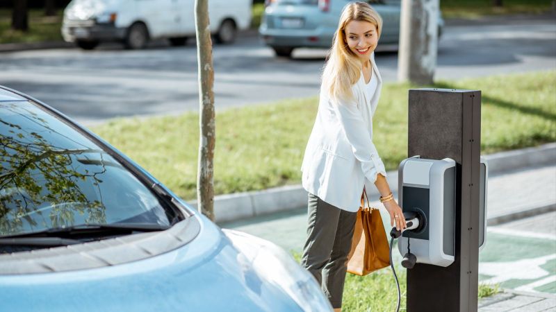 Das Bild zeigt eine Frau, die ein E-Auto an eine E-Säule anschließt zum 