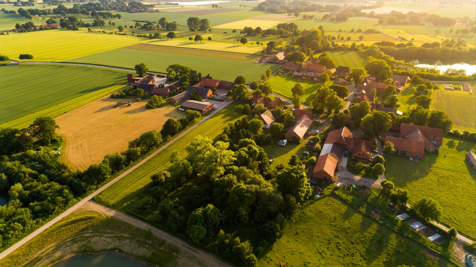 Eine Luftaufnahme einer Ortschaft in Deutschland. Zu sehen sind einige Häuser und Höfe, umringt von Feldern, Wiesen, Straßen und Seen.