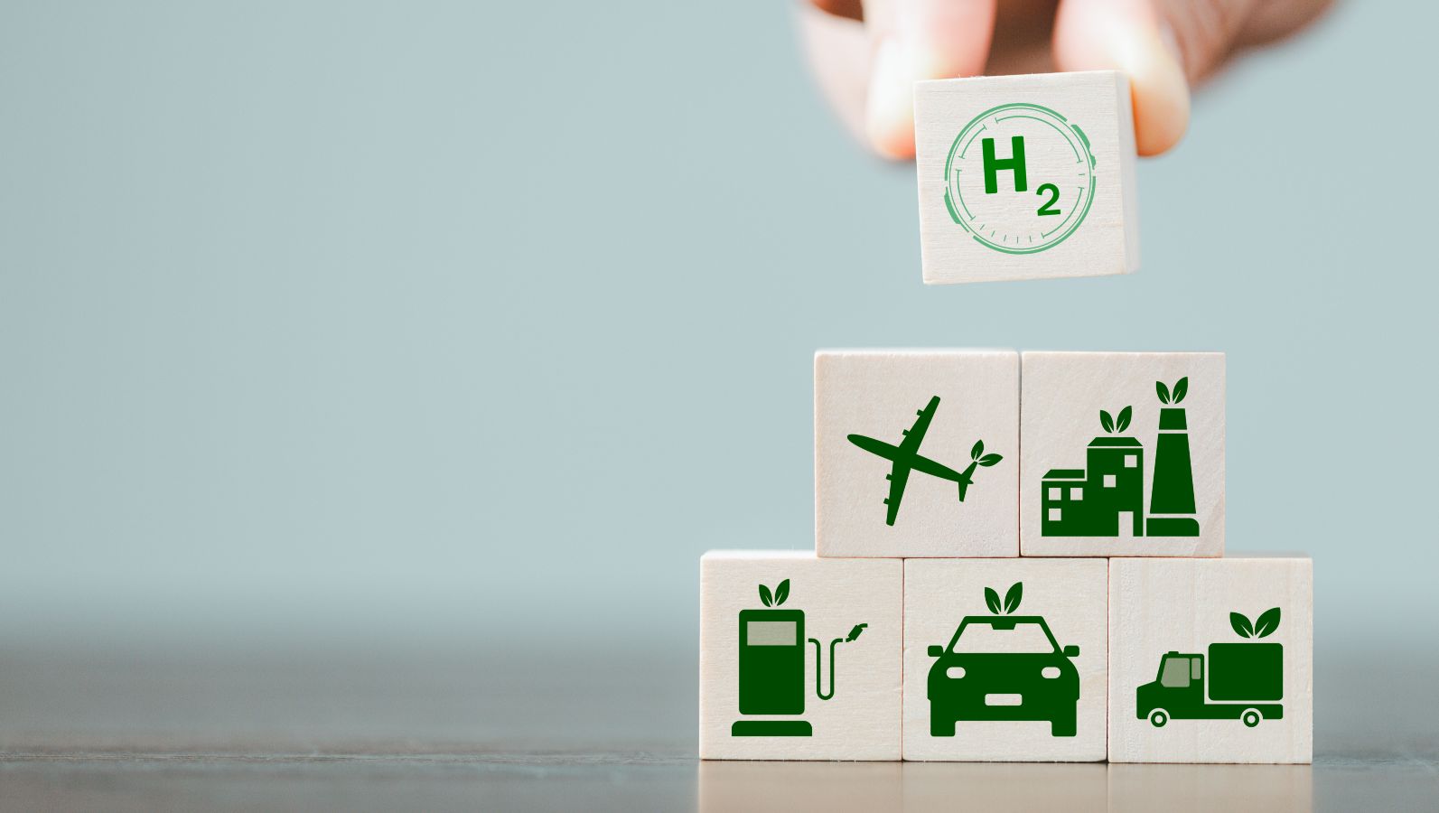 Zu sehen sind Spielsteine mit verschiedenen Symbolen, wie für Wasserstoff, nachhaltige Kraftstoffe, E-Mobilität und nachhaltiges Kerosin. Eine Hand baut damit eine Pyramide.