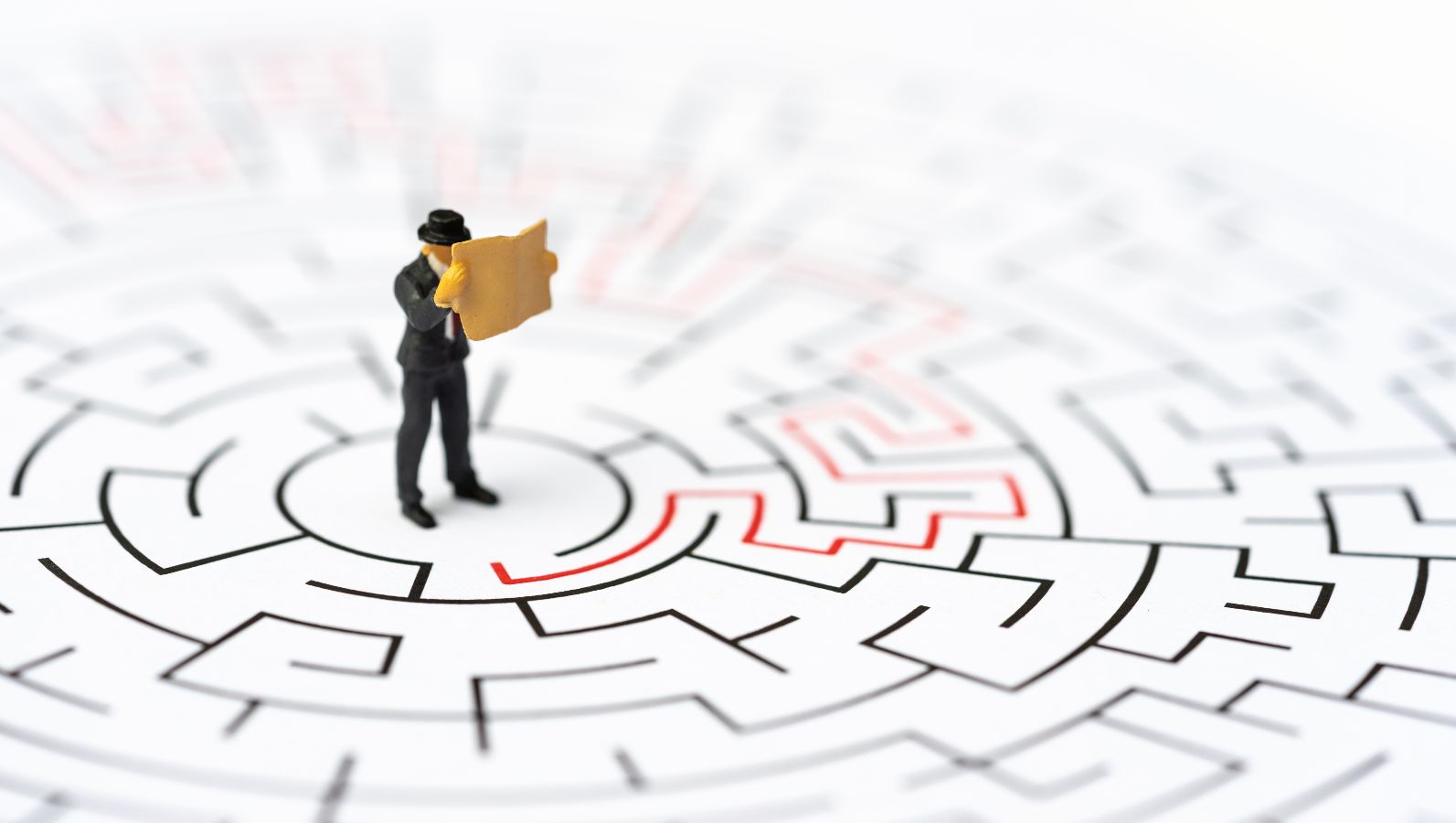 Das Bild zeigt eine Spielfigur, die inmitten eines Labyrinths steht und auf einer Karte Orientierung sucht.