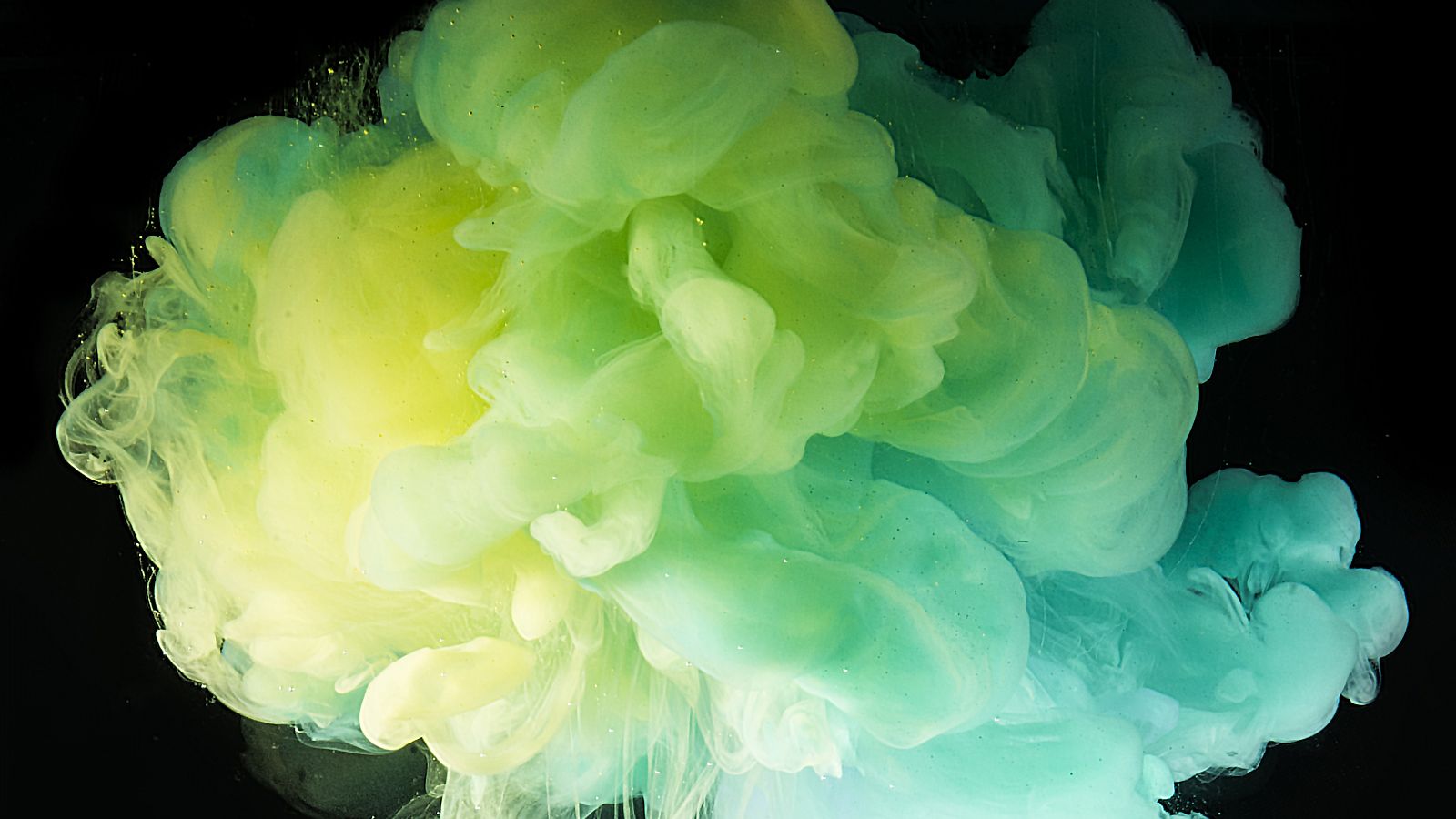 Das Foto zeigt eine aufsteigende grun-türkise Farbwolke in Wasser. 