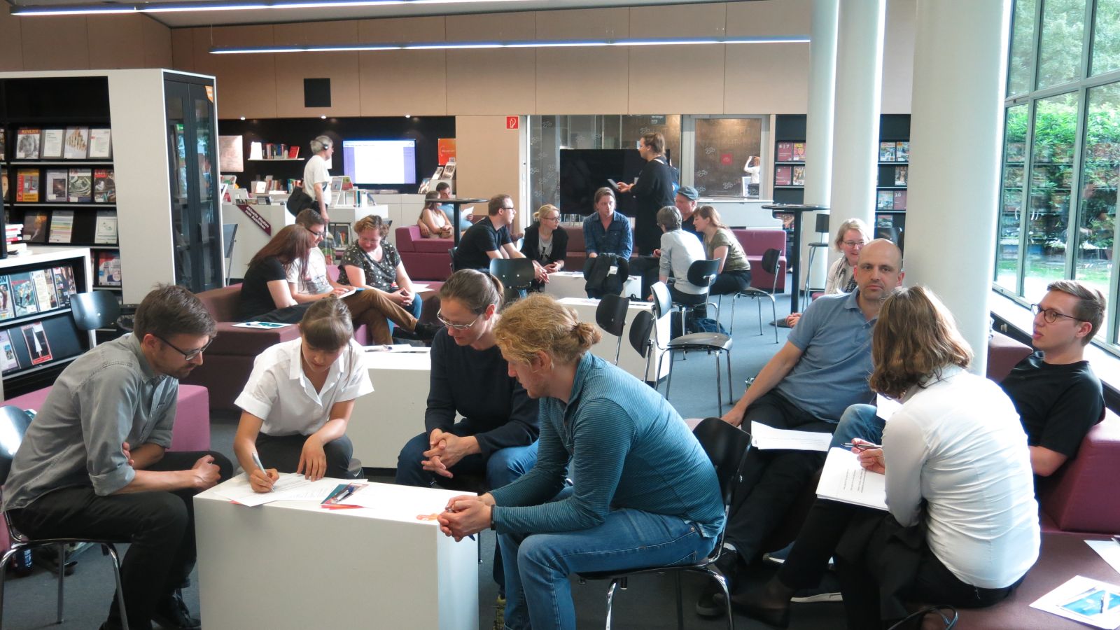 Das Bild zeigt eine Impression von einer Technologiecafé-Veranstaltung: mehrere, meist jüngere Menschen in einer Diskussions-Situation.