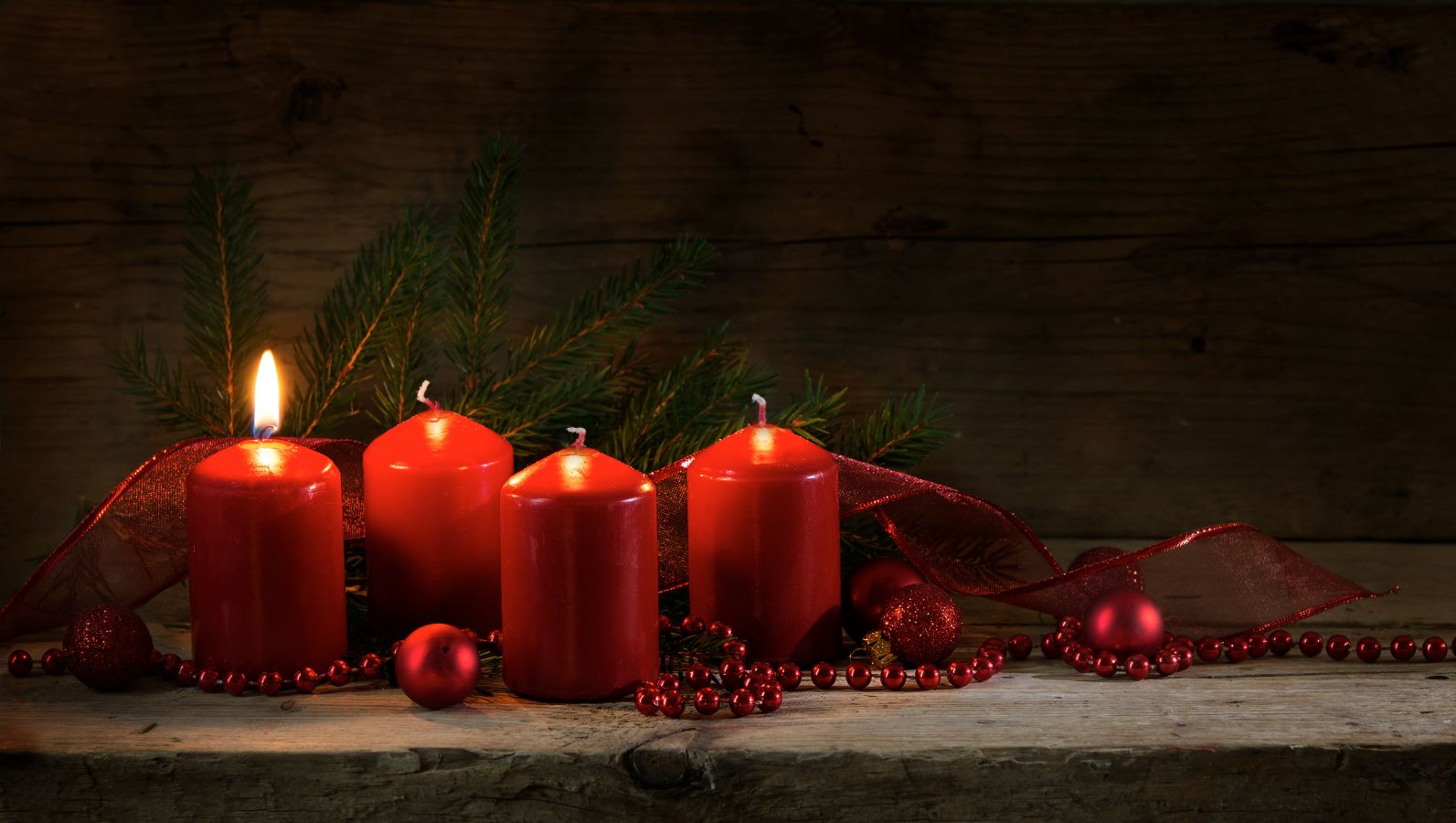 Zu sehen ist ein Adventsgesteck in der Farbe Rot mit vier Kerzen, von denen eine brennt.