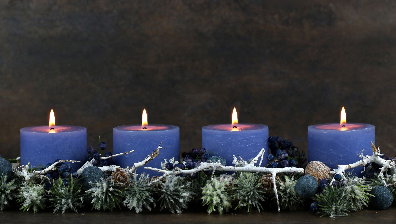 Zu sehen ist ein Adventsgesteck in der Farbwelt Blau mit vier Kerzen, von denen alle vier brennen.