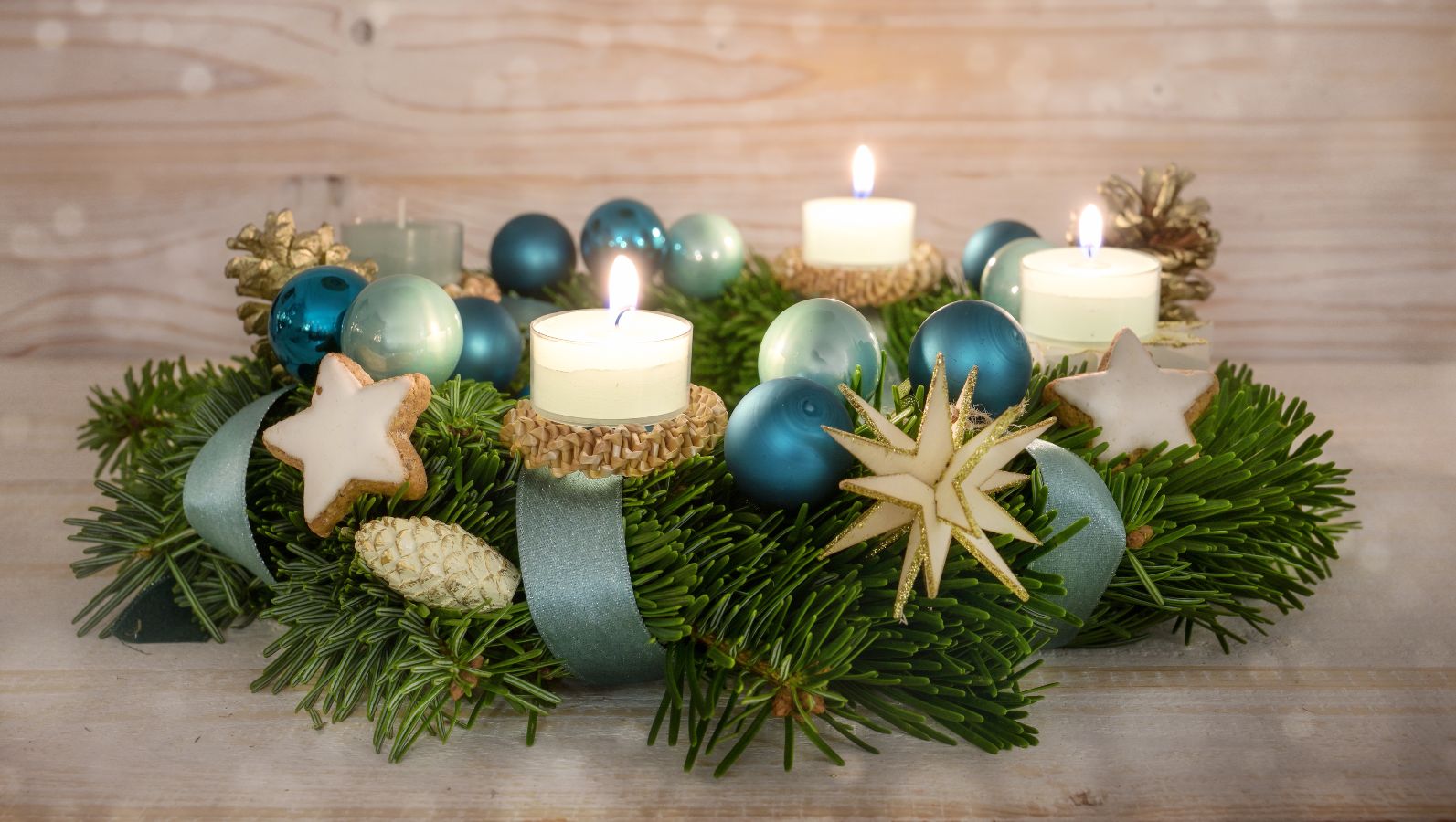 Zu sehen ist ein Adventsgesteck in der Farbwelt Blau-Türkis mit vier Kerzen, von denen drei brennen.