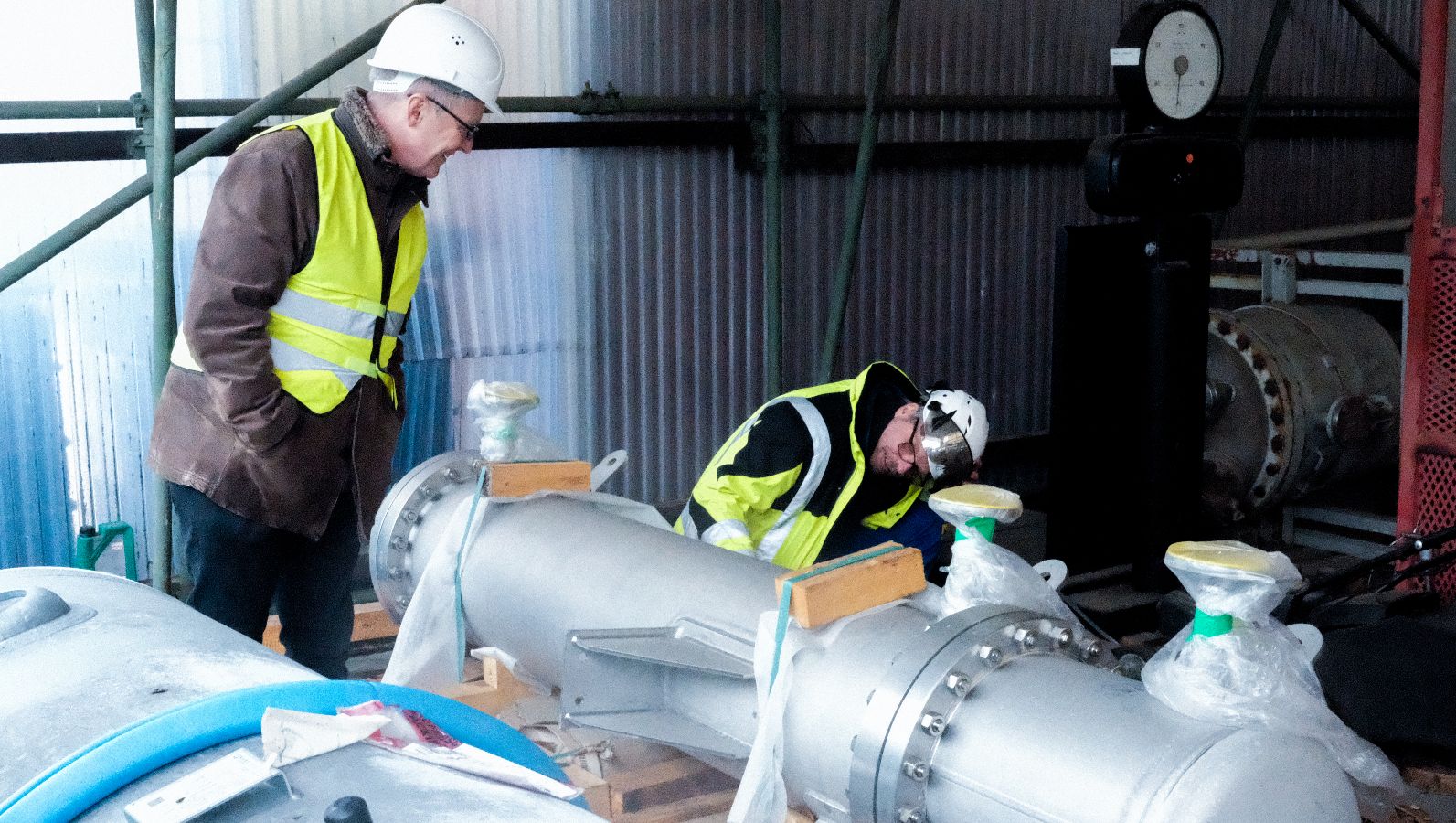 Das Foto zeigt zwei Männer in Schutzkleidung, die an einem Anlagenteil in Frankfurt-Höchst arbeiten.