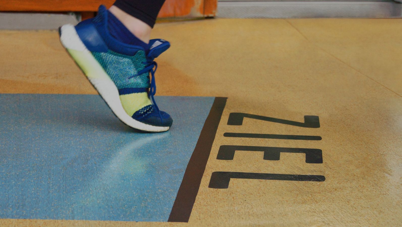 The photo shows the foot of a runner in running shoes taking the last step before reaching the finish line, marked by the German word ‘Ziel’ for finish.