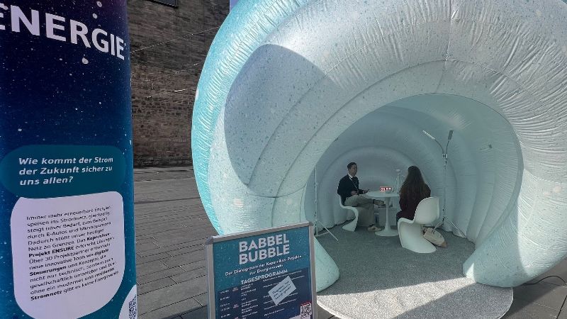 Das Bild zeigt die Babbel Bubble auf einem Marktplatz. Im Inneren sitzen sich zwei Leute gegenüber.