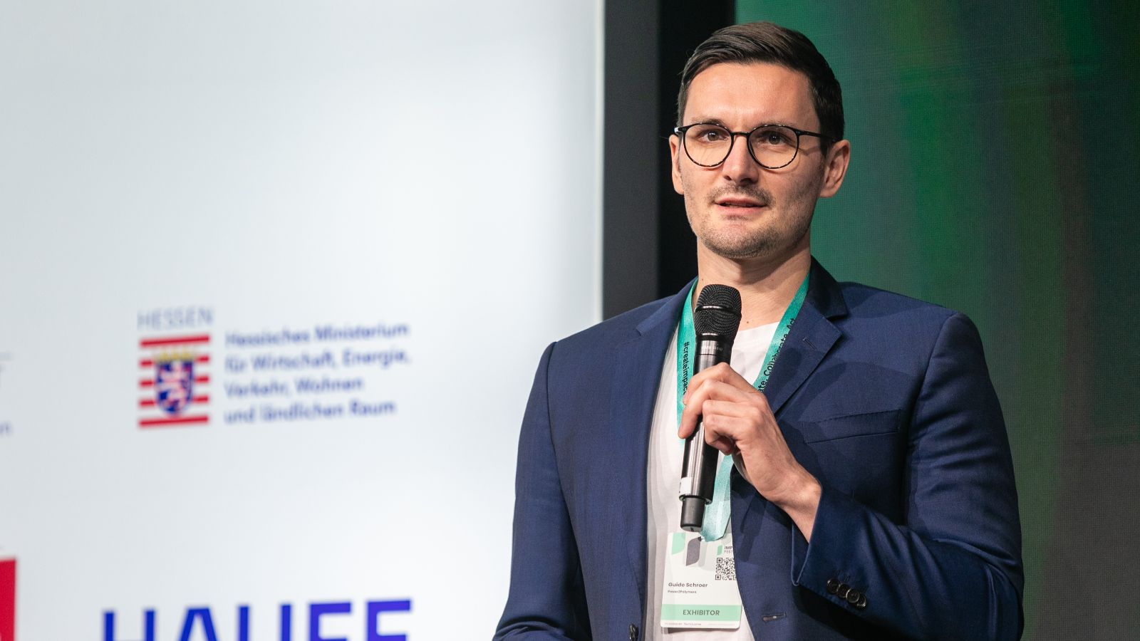 Man sieht einen Mann mit Mikrofon auf einer Bühne.