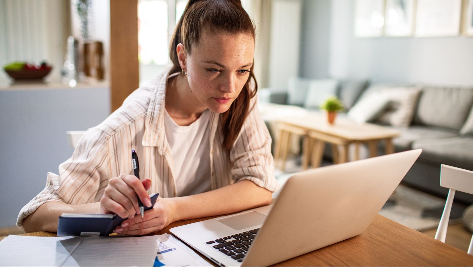 Das Bild zeigt eine Frau, die vor inem aufgeklappten Laptop sitzt und auf dessen Bildschirm etwas konzentriert anschaut.