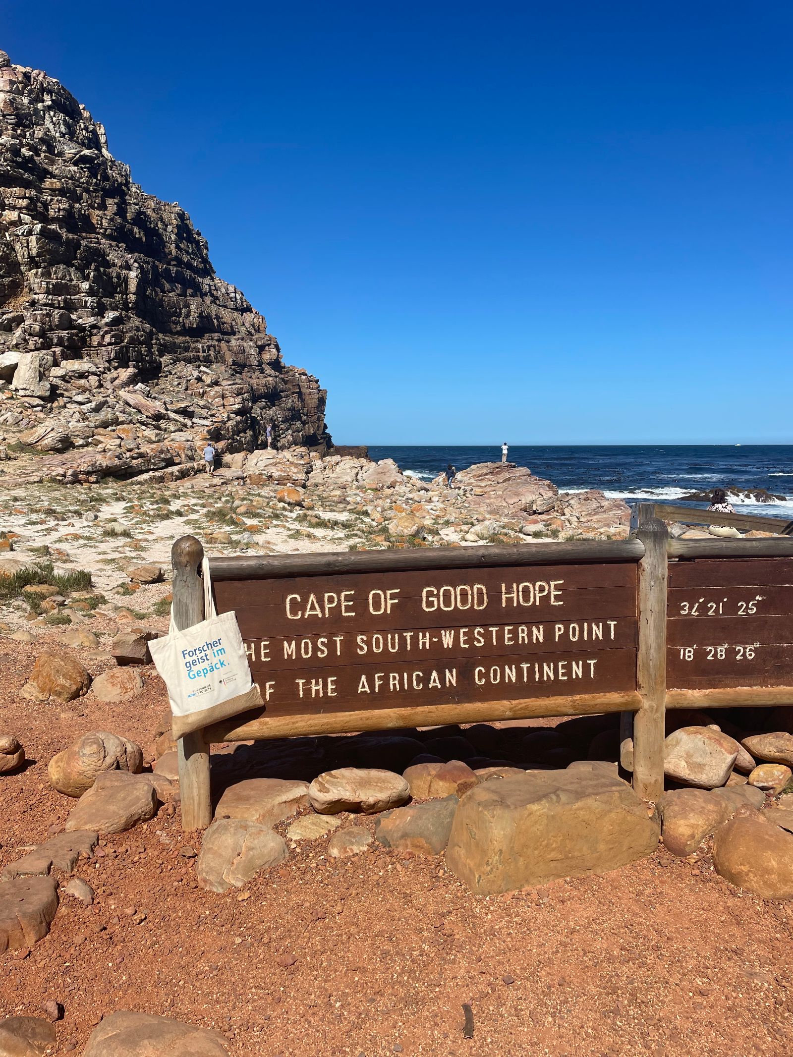 Zu sehen ist ein Schild vor Landschaft und Meer, auf dem auf Englisch 
