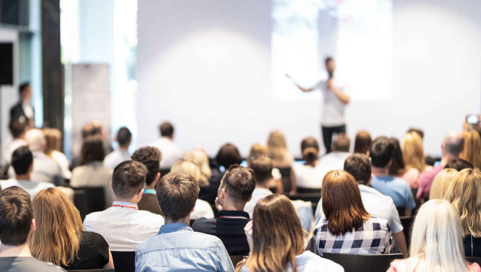 Image of a conference presentation with a view of the speaker on the podium.