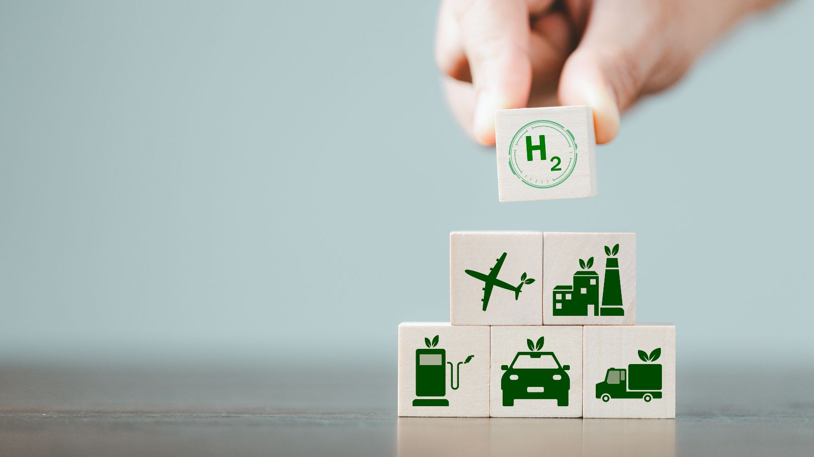 Zu sehen sind Spielsteine mit verschiedenen Symbolen, wie für Wasserstoff, nachhaltige Kraftstoffe, E-Mobilität und nachhaltiges Kerosin. Eine Hand baut damit eine Pyramide.